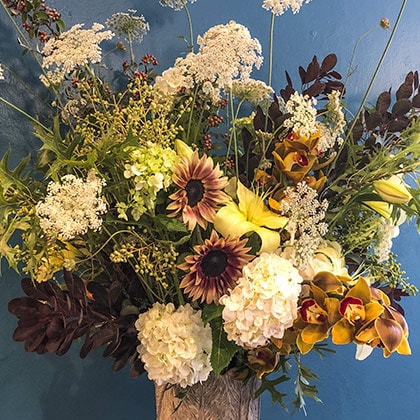 This tall flower arrangement of Queen Anne&rsquo;s lace, privet berries, sunflowers, cymbidium orchids, hydrangeas, yellow lilies and brown cotinus foliage made quit a splash with our customer. 