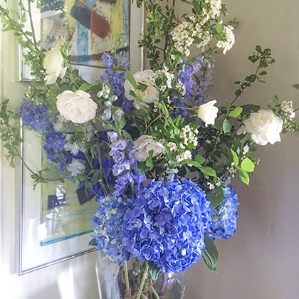Spring is welcomed by white Hawrhorne branches and blue delphinium mixed with Iceberg roses and a beautiful shade of blue hydrangea complete this flower arrangement.