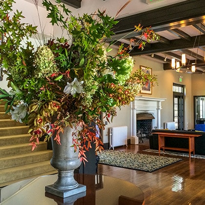 A large entry flower arrangement filled with hydrangeas, white Casa Blanca lilies, tall oak leaves, colorful nandina, pistachio berries and red crocosmia.